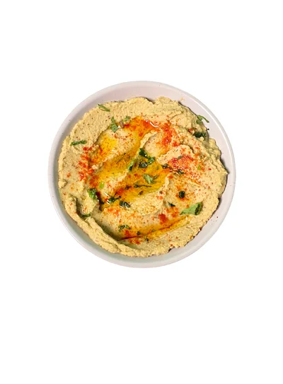 A white bowl of smooth hummus swirled with olive oil, Kashmiri chilli powder and chopped coriander