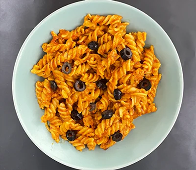 A pale green bowl of fusilli in a thick orange-red tomato sauce, topped with sliced black olives
