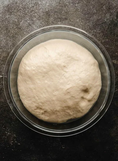 A smooth ball of chapati dough in a glass bowl, seen from above
