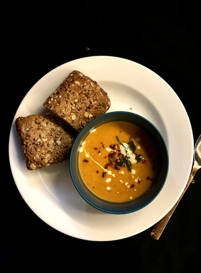 A bowl of orange tomato soup with a cream swirl and crisp garlic, next to two slices of seeded bread