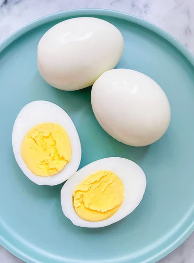 Two whole peeled boiled eggs and two halves with firm yellow yolks on a pale blue plate