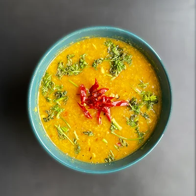 A teal bowl of yellow moong dal fry topped with chopped coriander and red chilli