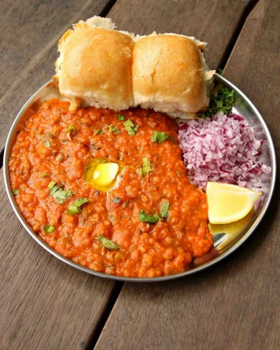 A steel plate of pav bhaji with butter-toasted pav, chopped onion and lemon